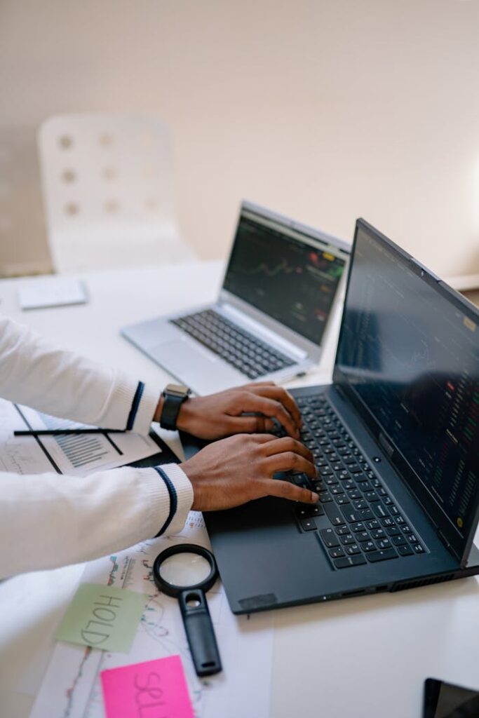 A person working on two laptops with financial charts, emphasizing remote productivity.
